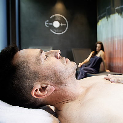 Muž odpočívající na lehátku, v pozadí žena v relaxační místnosti.